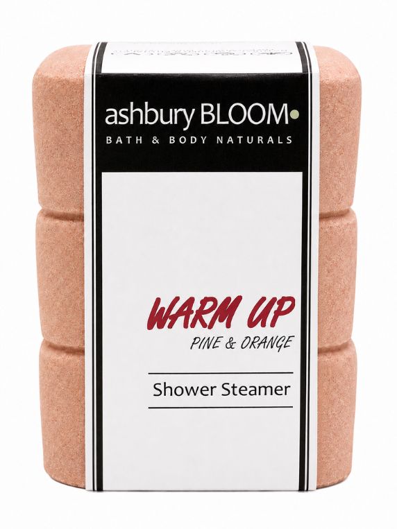 Ashbury Bloom Warm Up Pine & Orange shower steamers stacked in their branded packaging, displayed with fresh evergreen branches and an orange slice.